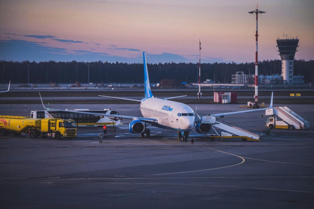 Jet airplane parked at airport tarmac during twilight with refueling trucks and boarding stairs
