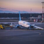 Jet airplane parked at airport tarmac during twilight with refueling trucks and boarding stairs