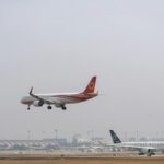Two commercial airplanes approaching landing at a busy international airport with control tower visible.
