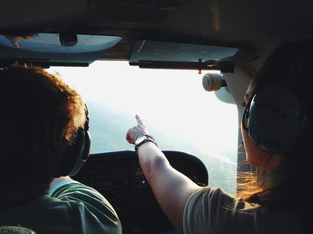 Two people in a small aircraft cockpit, navigating with headsets during a daytime flight.