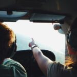 Two people in a small aircraft cockpit, navigating with headsets during a daytime flight.